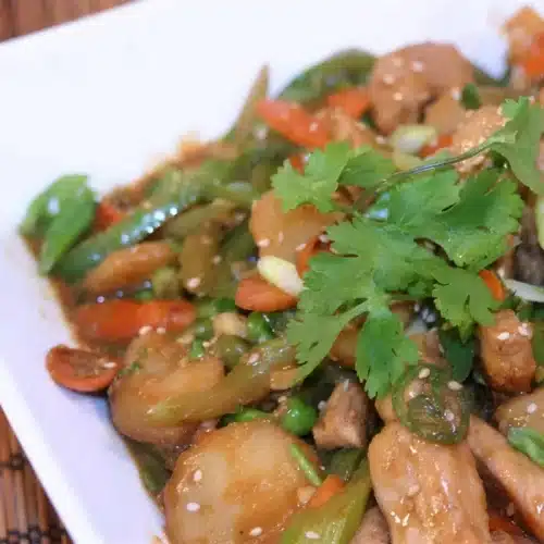 Spicy pork stir fry served over rice with cilantro and sesame seeds