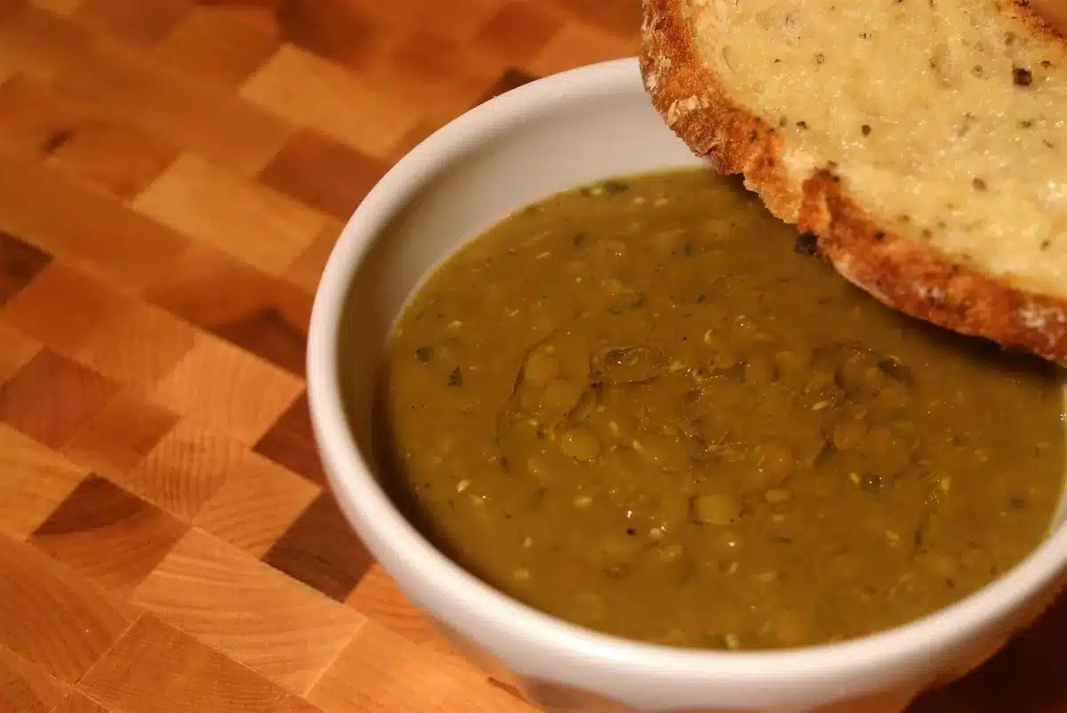 Rustic white bowl of thick green stew on a wooden board with toasted bread