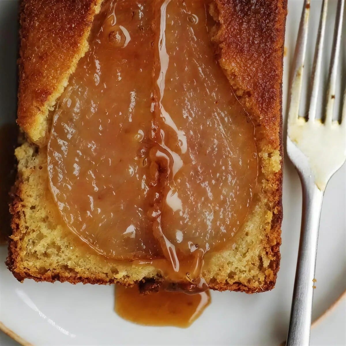 Dark caramel running off a golden slice onto a rimmed plate beside a fork