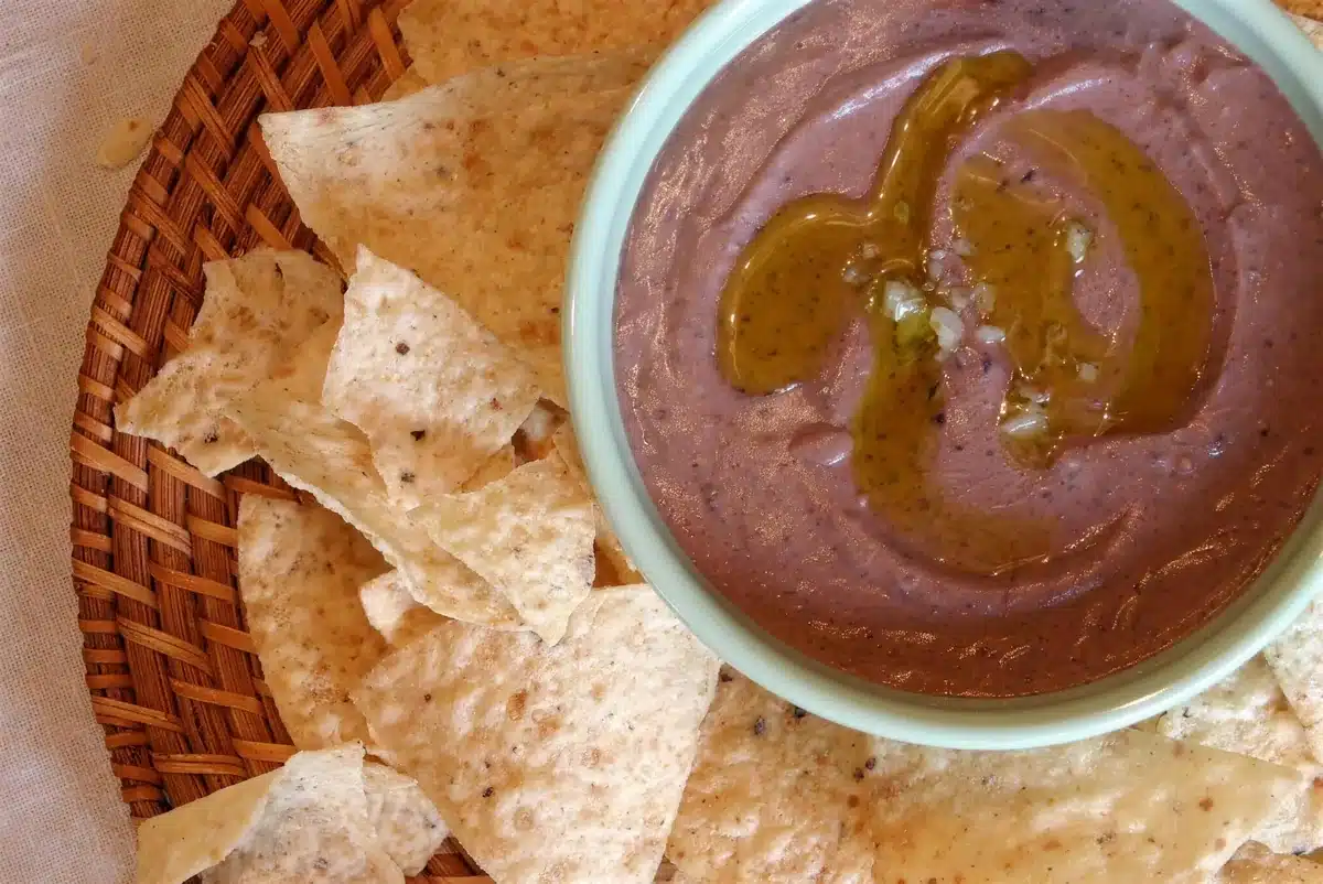 Black bean hummus in a bowl with tortilla chips on a woven tray