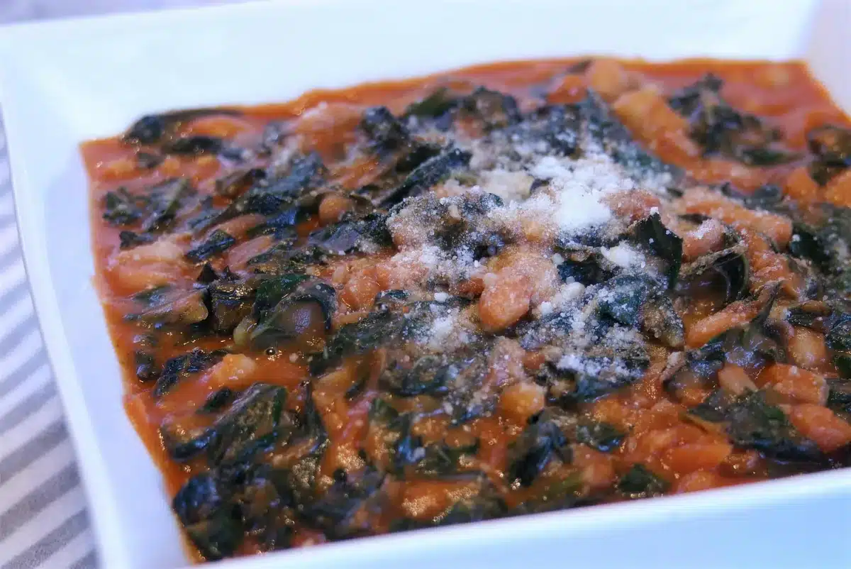 Braised kale and white beans in a white baking dish under grated cheese