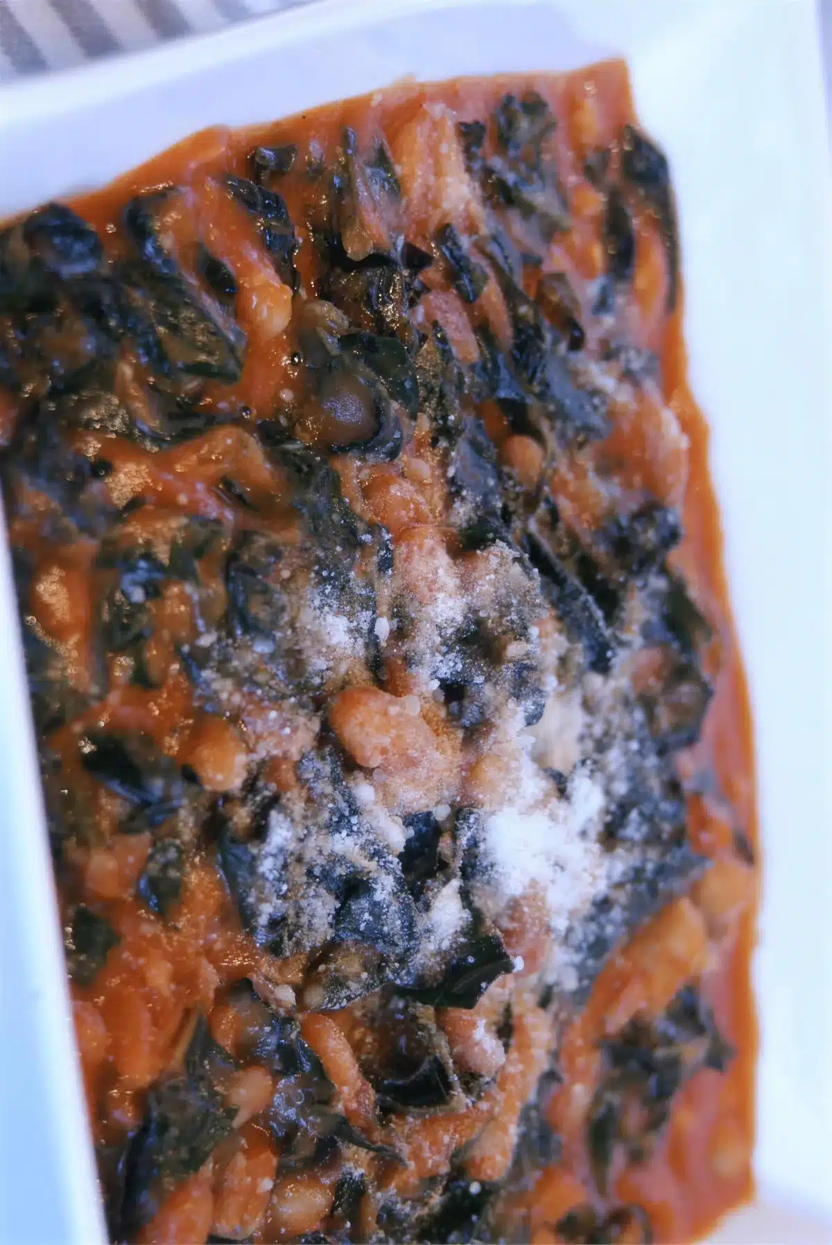 Braised kale and cannellini beans in tomato sauce topped with grated parmesan