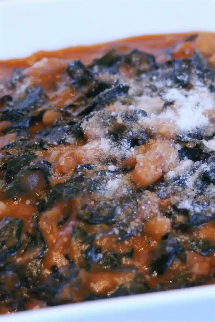 Close view of white beans and dark greens under a dusting of cheese