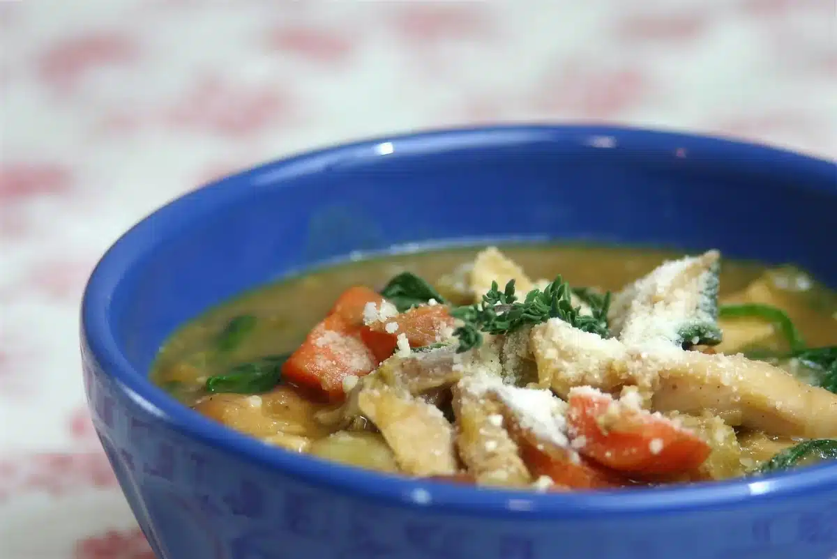 Blue bowl on a red floral cloth beside a spoon of golden broth