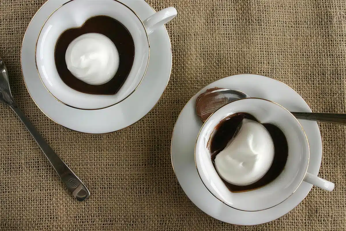 Two gold rimmed cups of dark custard on burlap with spoons