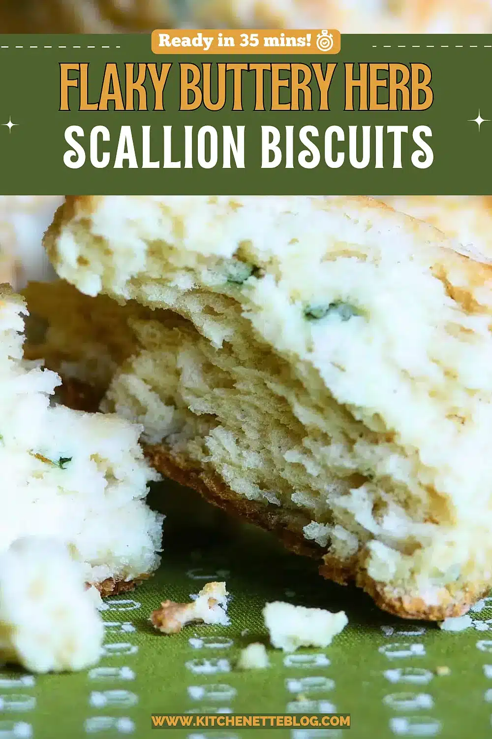 A split buttermilk biscuit showing its flaky steaming interior flecked with green onion, resting on a green cloth