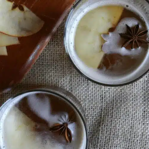 Two short glasses seen from above with star anise floating on the foam