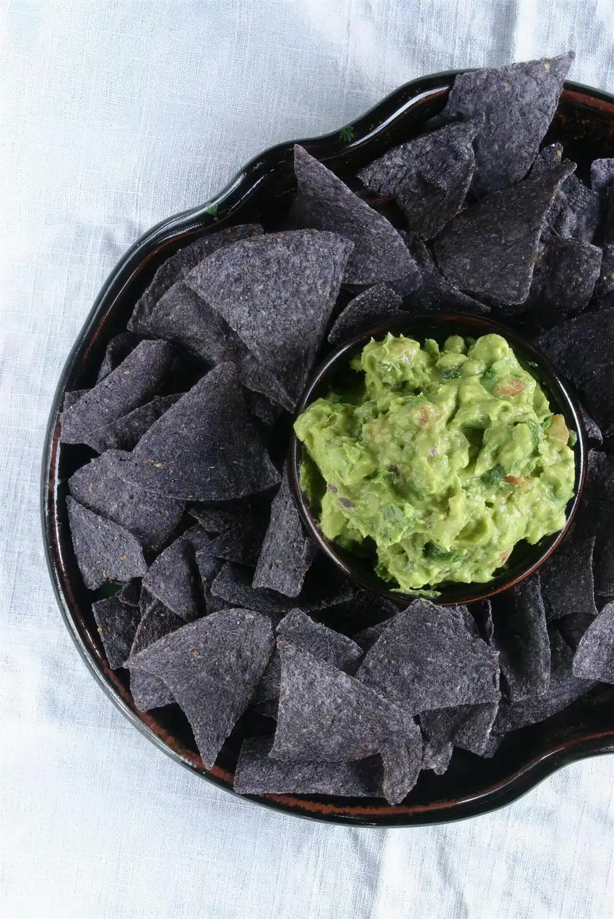 Spicy guacamole in a dark bowl ringed with blue corn tortilla chips