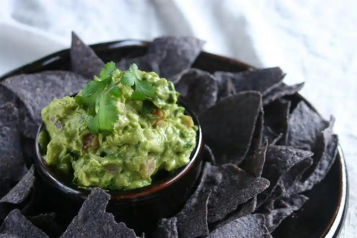 Blue corn chips fanned around a bowl of pale green dip