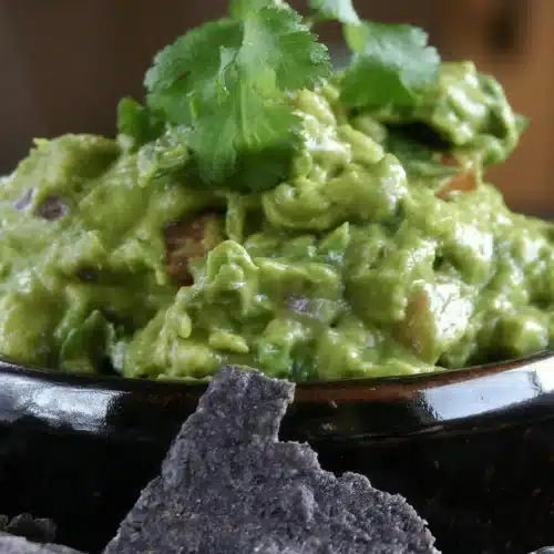 Spicy guacamole heaped in a black bowl and topped with cilantro