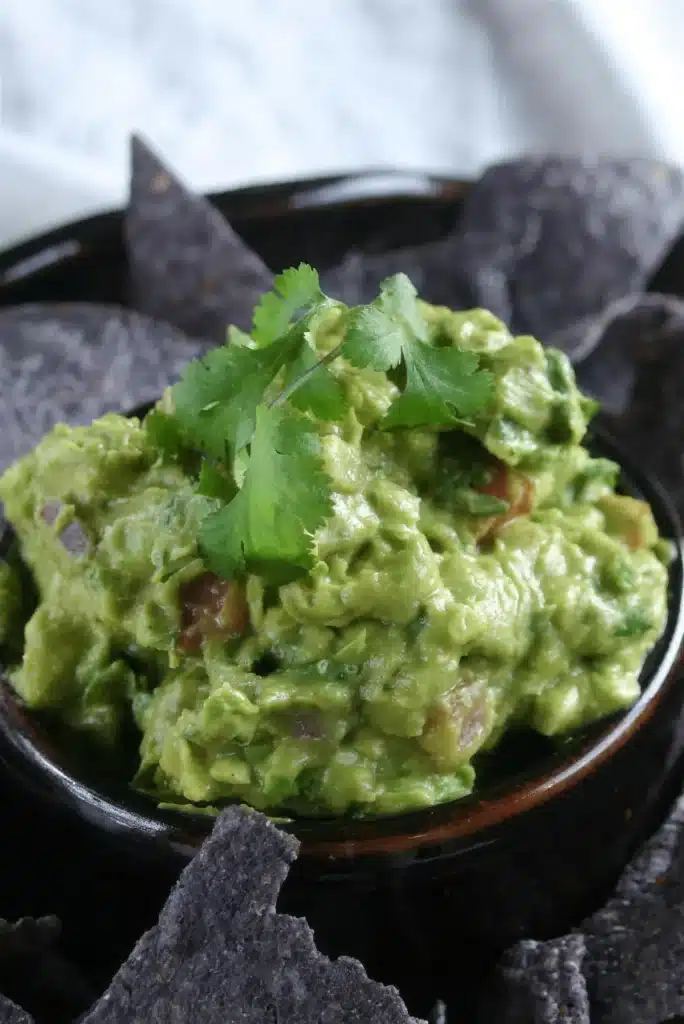 A black bowl of chunky green dip topped with cilantro leaves