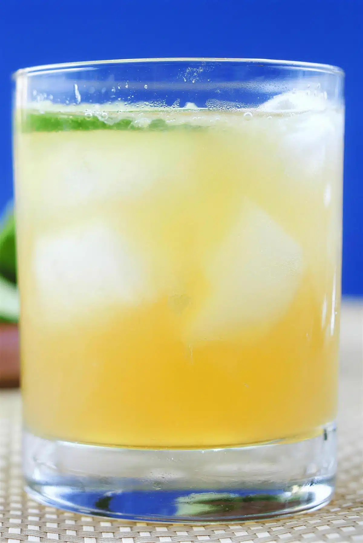 Tall glass of a pale iced drink with large cubes against a deep blue background