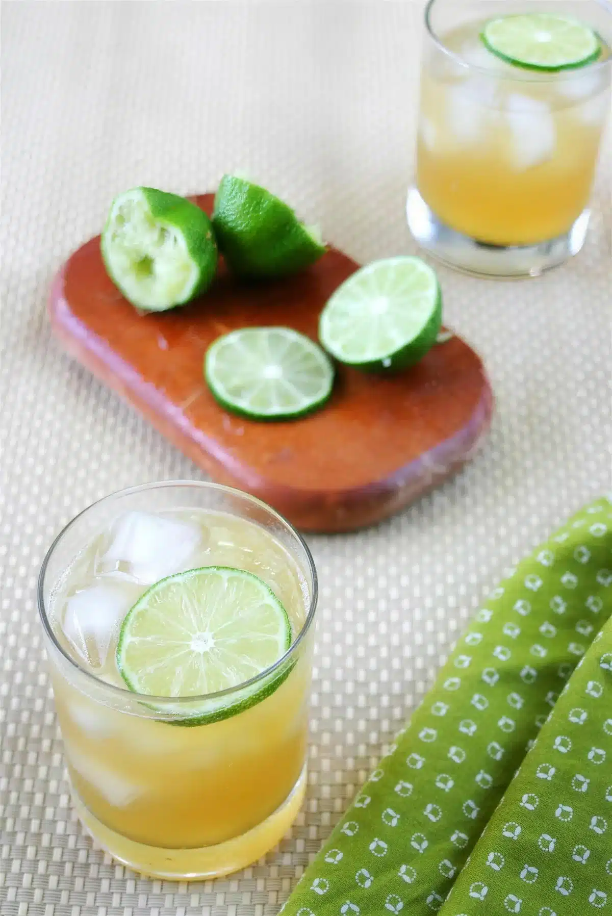 Halved limes on a wooden board beside two filled glasses on a woven mat