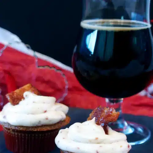 Maple bacon cupcakes on slate beside a stemmed glass of dark beer