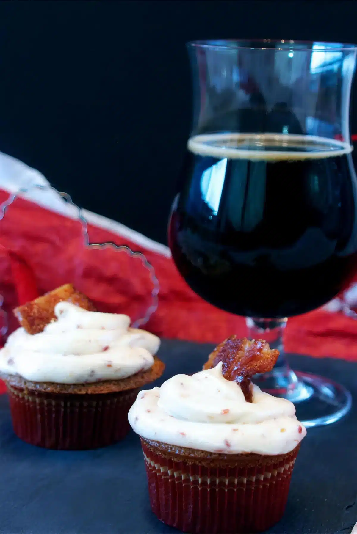 Maple bacon cupcakes on slate beside a stemmed glass of dark beer