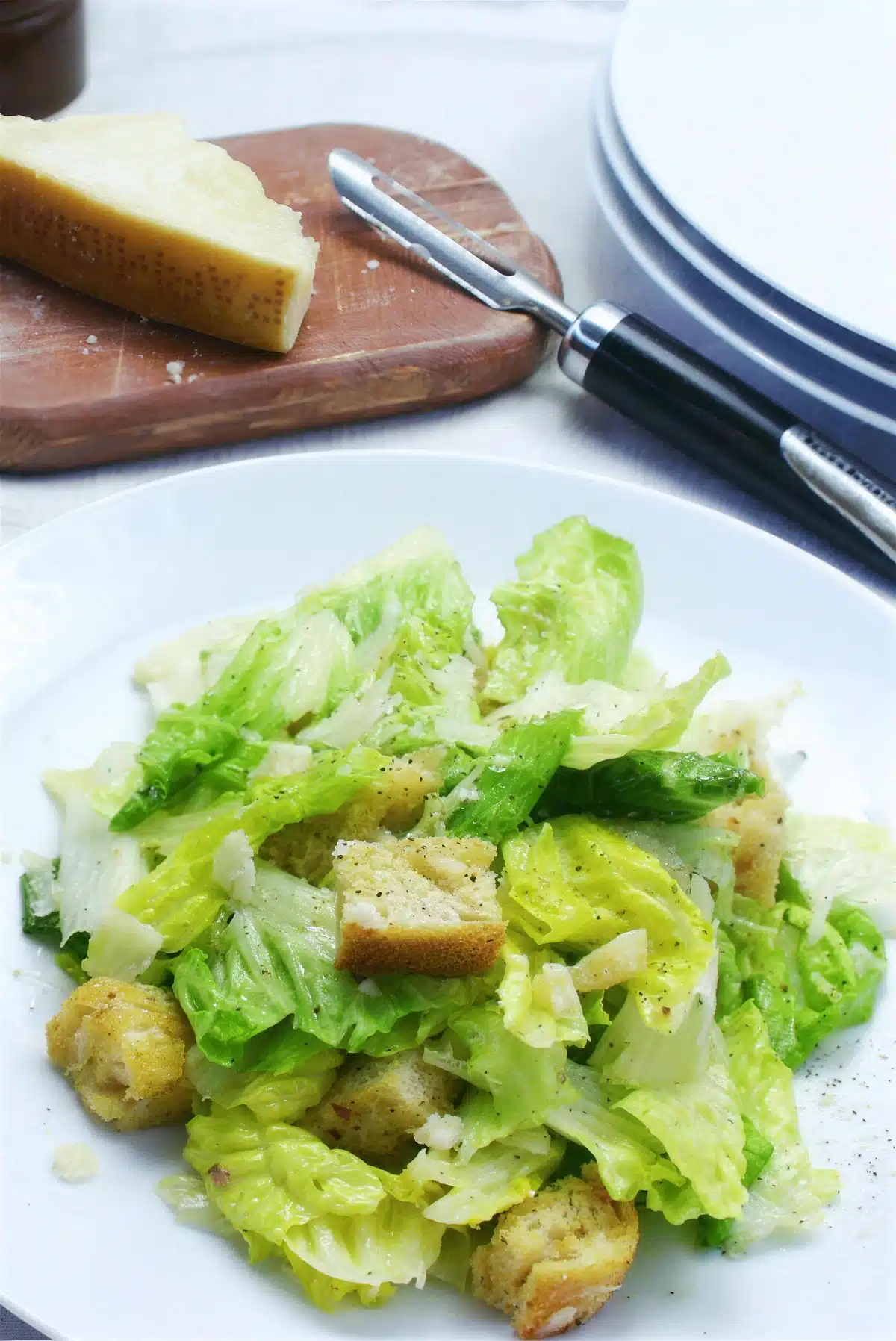Lemon caesar salad on a white plate with a parmesan wedge behind
