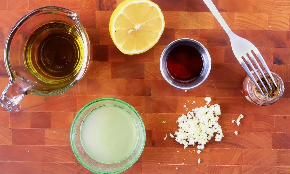 Olive oil, a halved citrus, red wine vinegar and garlic laid out on a wooden board