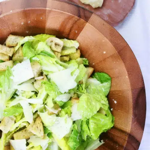 Lemon caesar salad tossed in a large wooden bowl with shaved parmesan