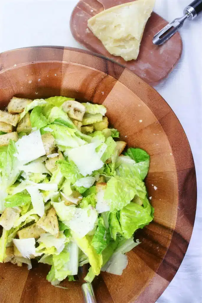 Lemon caesar salad tossed in a large wooden bowl with shaved parmesan