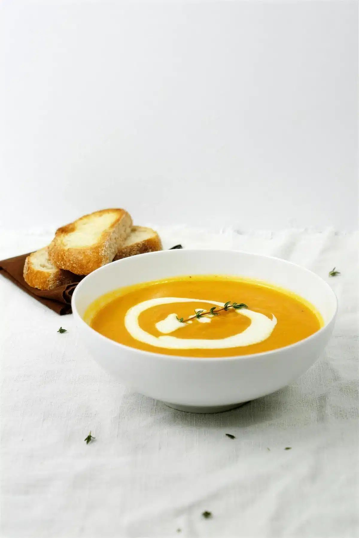 Carrot parsnip soup in a white bowl with toasted bread slices behind it