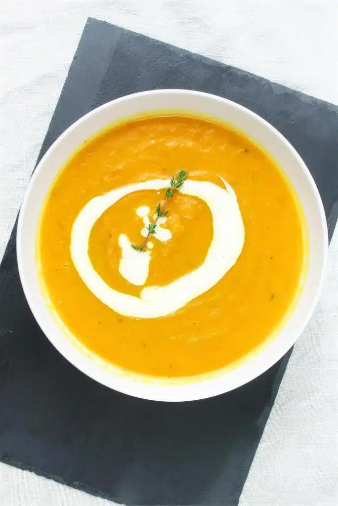 Carrot parsnip soup photographed from above on a dark slate board with a thyme sprig