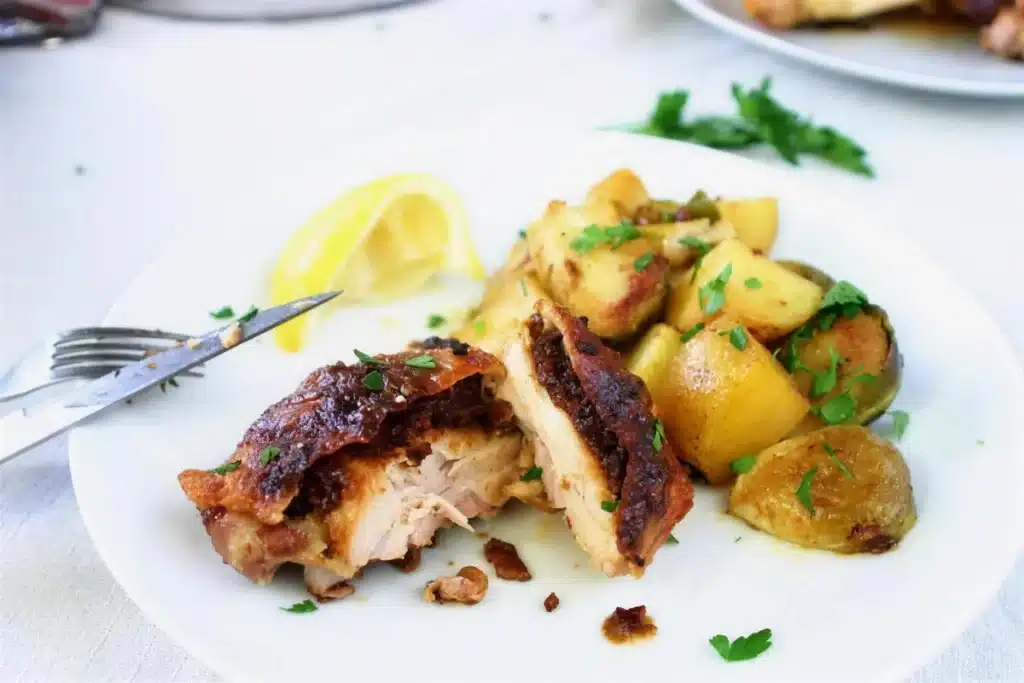 Crisp-skinned thigh cut open on a white plate with baby potatoes and parsley