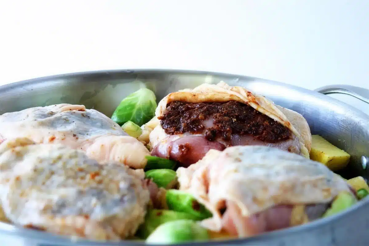 Bacon jam being spread under the skin of a raw thigh in a metal pan
