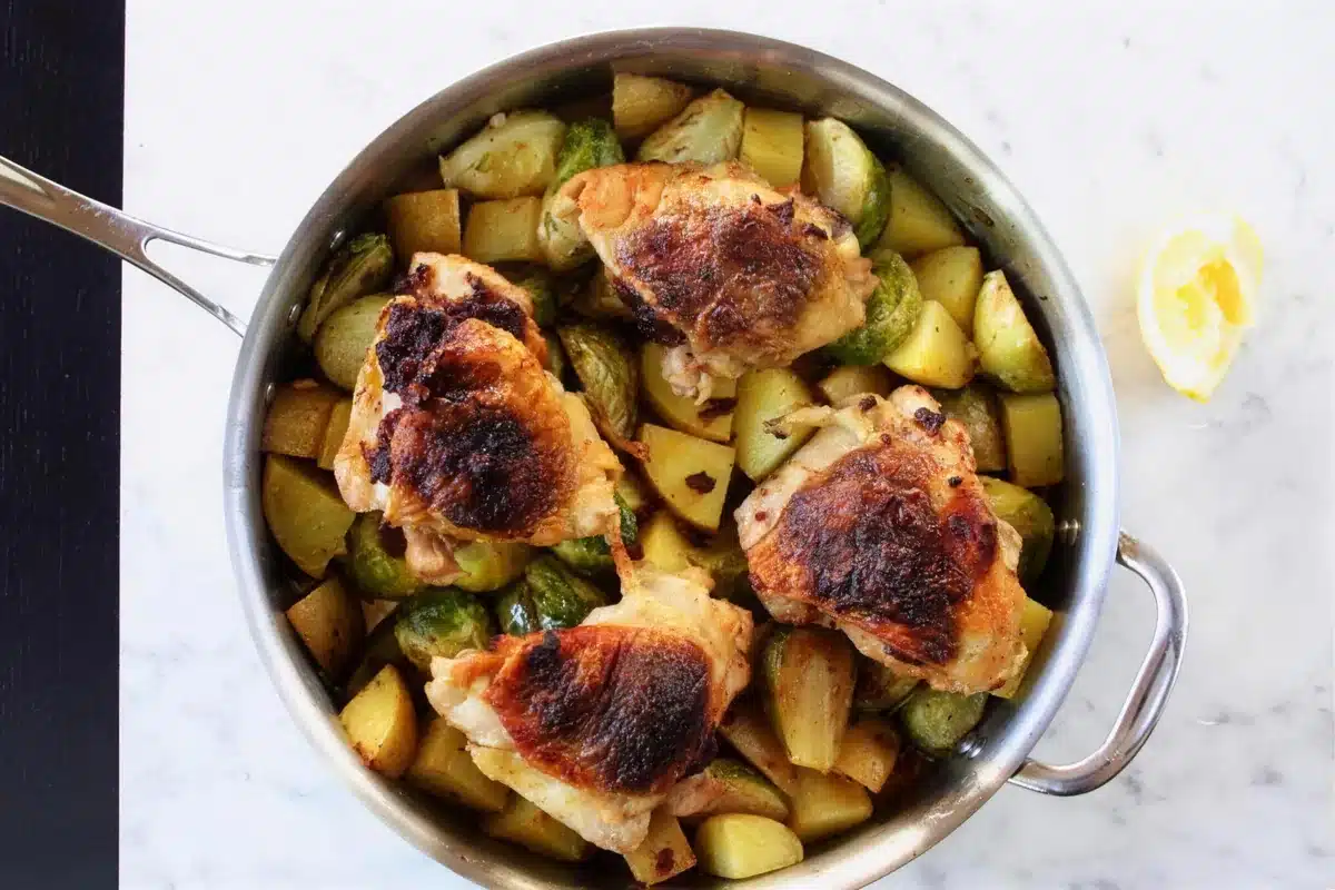 Roasted chicken and vegetables in a steel pan, skin side up over browned potato chunks
