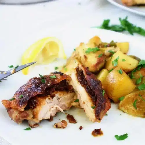 Crisp-skinned thigh cut open on a white plate with baby potatoes and parsley