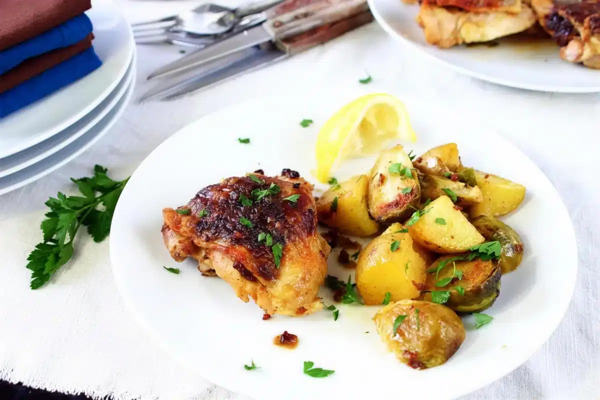 Golden thigh and buttery potato chunks on a white plate with a lemon wedge
