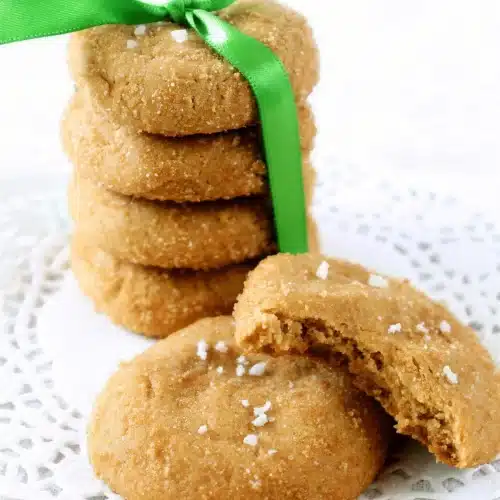 Butterscotch cookies stacked on a doily with one broken open to show the chewy middle