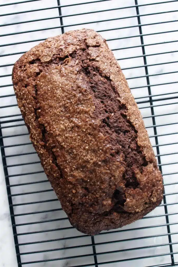 Whole dark loaf with a sugared crust cooling on a wire rack