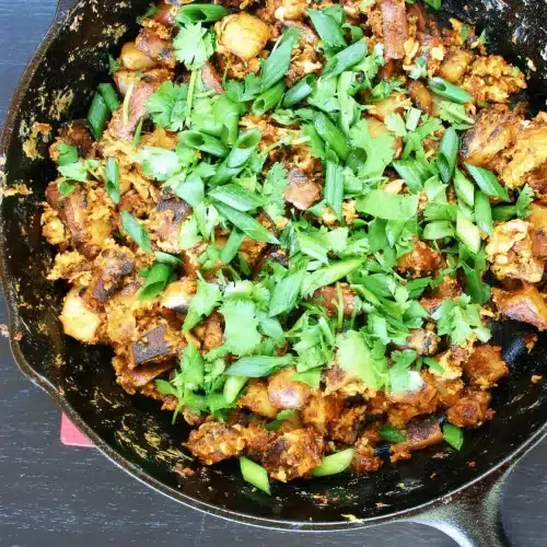 Chorizo hash in a cast iron skillet under scallions and cilantro