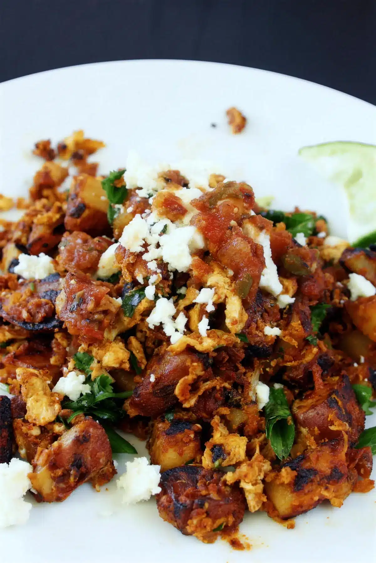 A mound of browned potatoes and egg on a white plate with a lime slice
