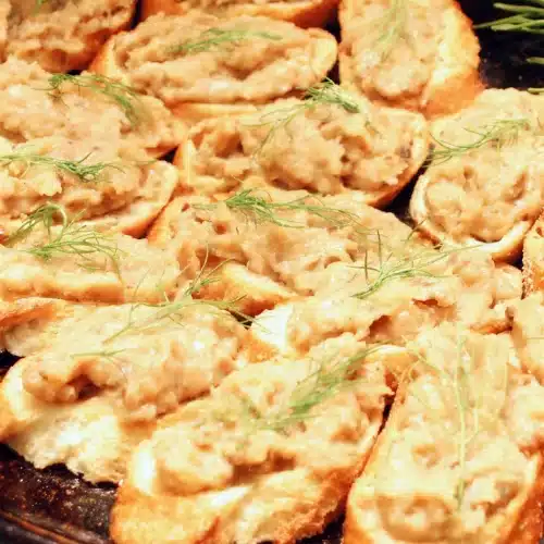 White bean crostini crowded onto a dark platter with fennel fronds