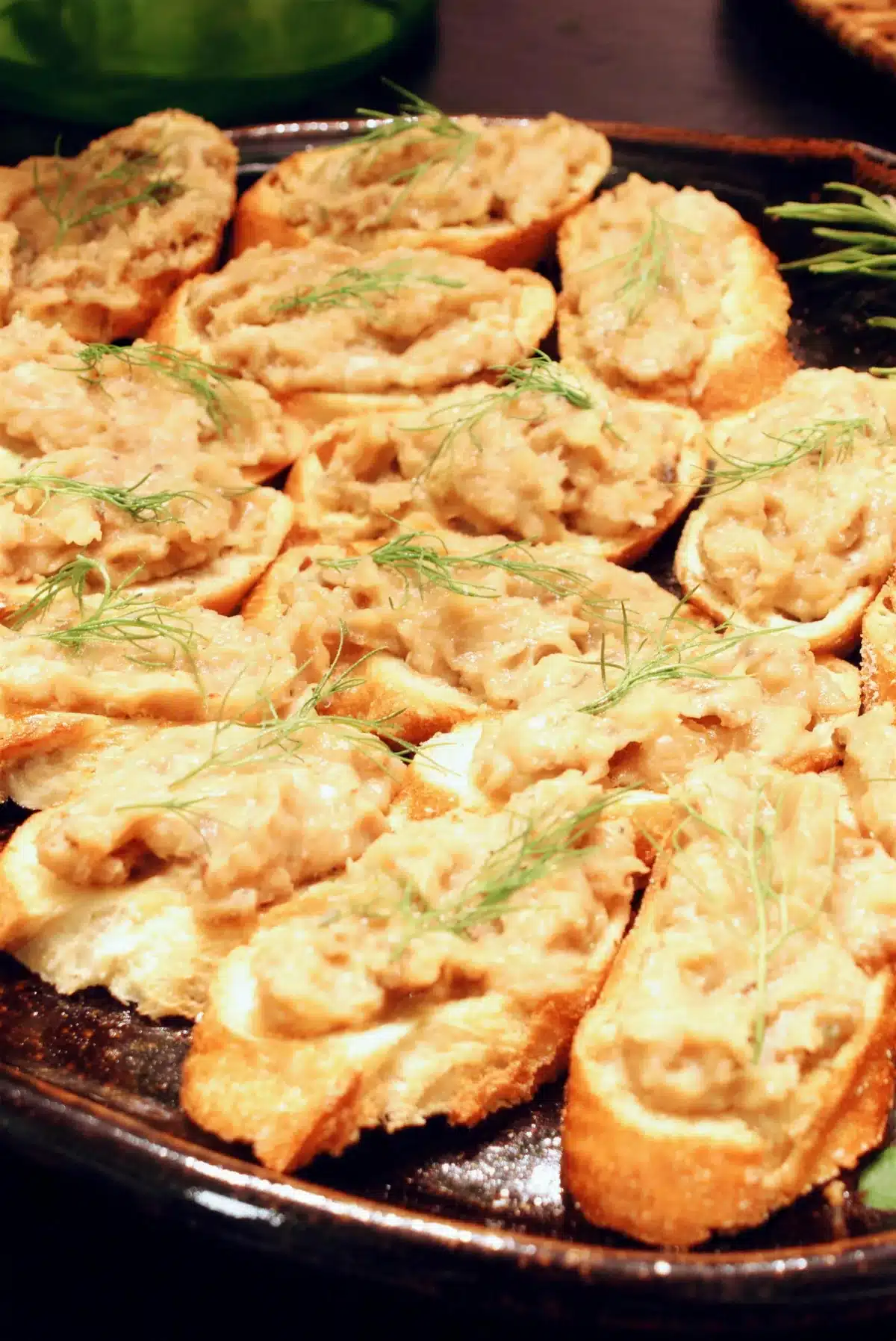 White bean crostini crowded onto a dark platter with fennel fronds