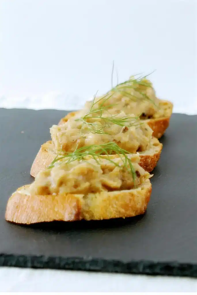 A single toast piled high with pale spread and a green frond on slate