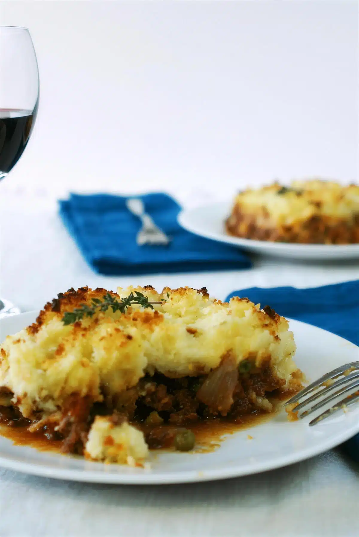 Serving of shepherds pie on a white plate with red wine alongside