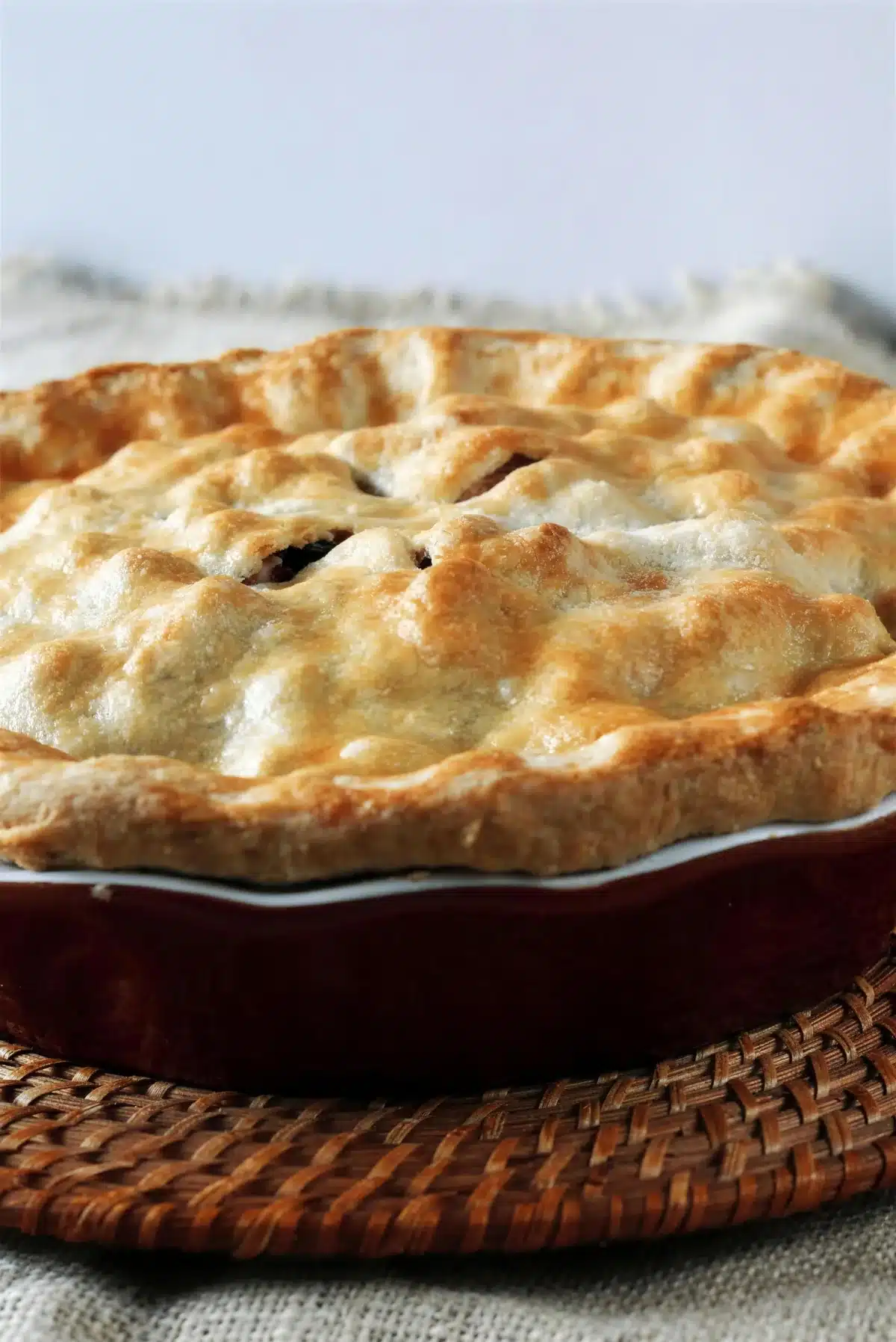 Blueberry rhubarb pie baked whole in a red dish on a woven mat