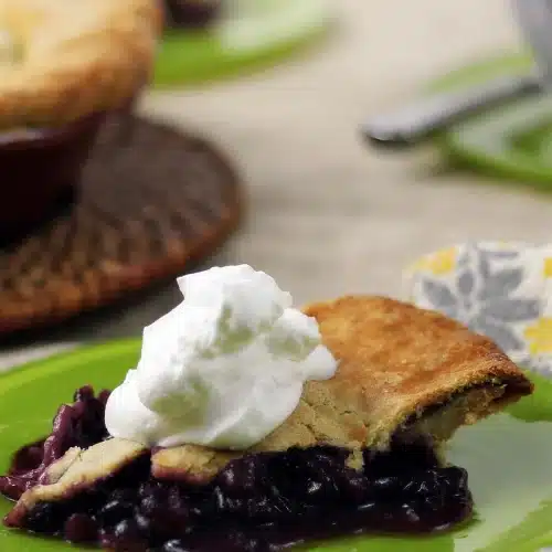 Blueberry rhubarb pie slice on a green plate with a spoon behind
