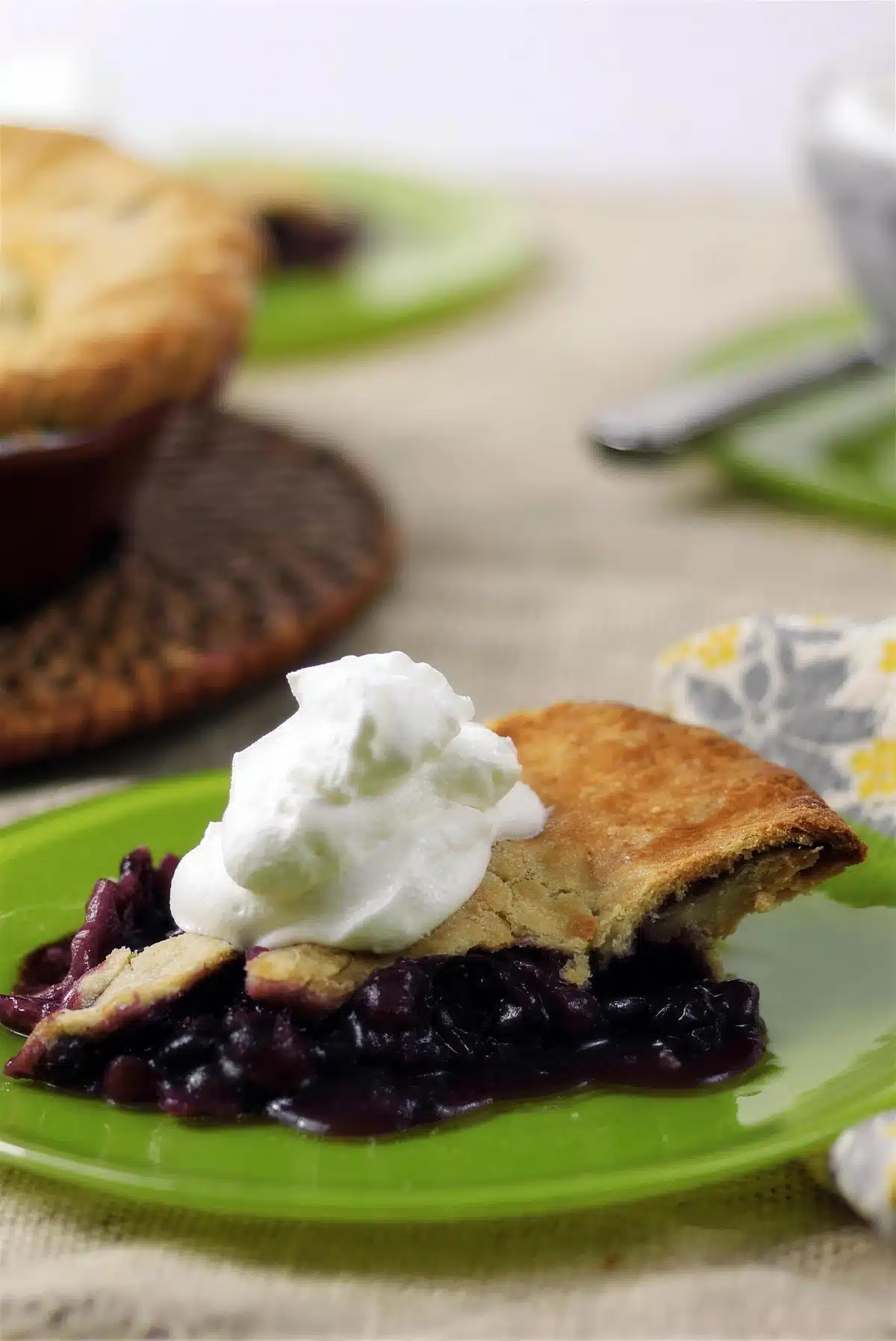 Blueberry rhubarb pie slice on a green plate with a spoon behind