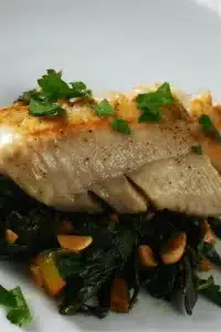 Pan seared cod with rainbow chard and almonds on a white plate
