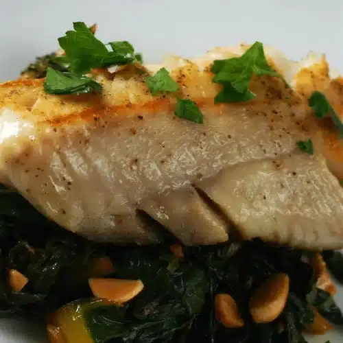 Pan seared cod with rainbow chard and almonds on a white plate