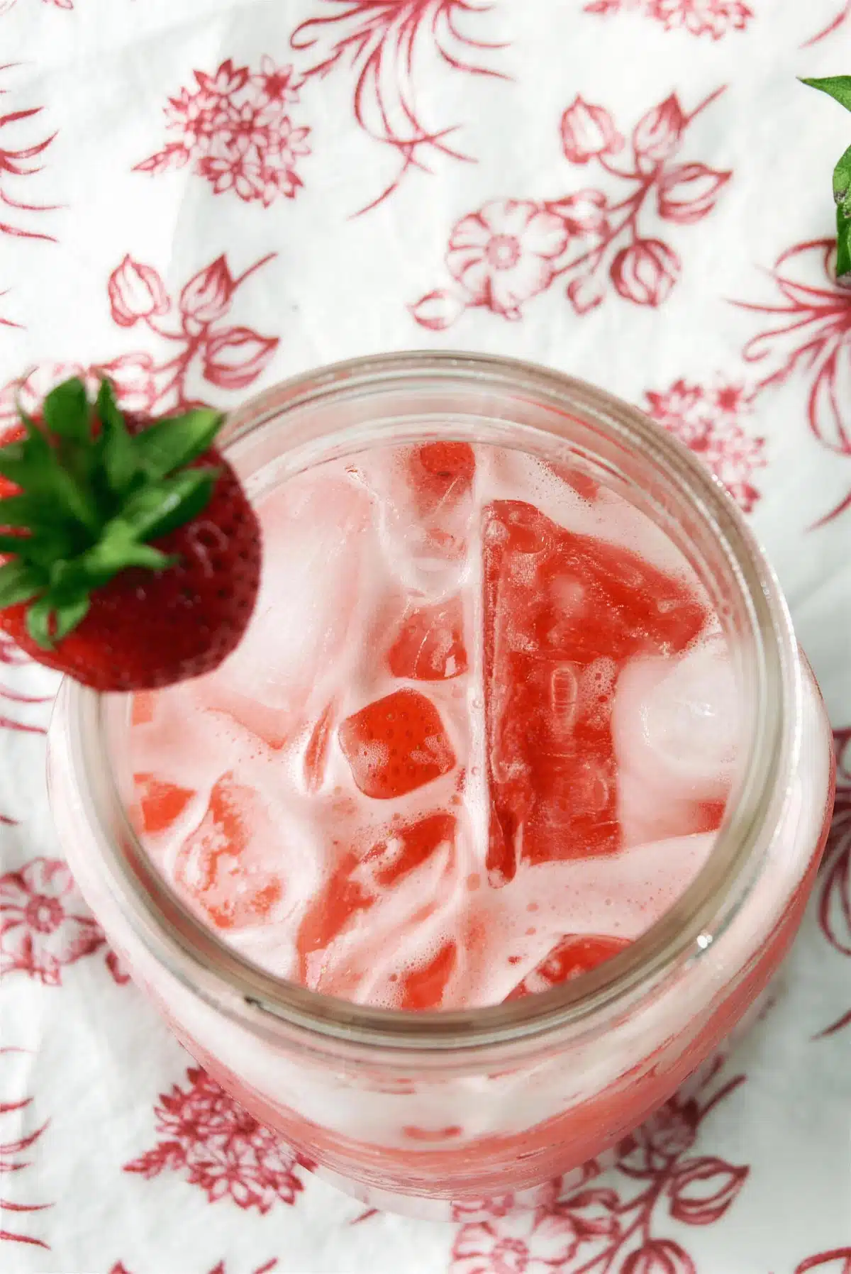 Strawberry syrup and soda water in a jar seen from above with fruit on the rim