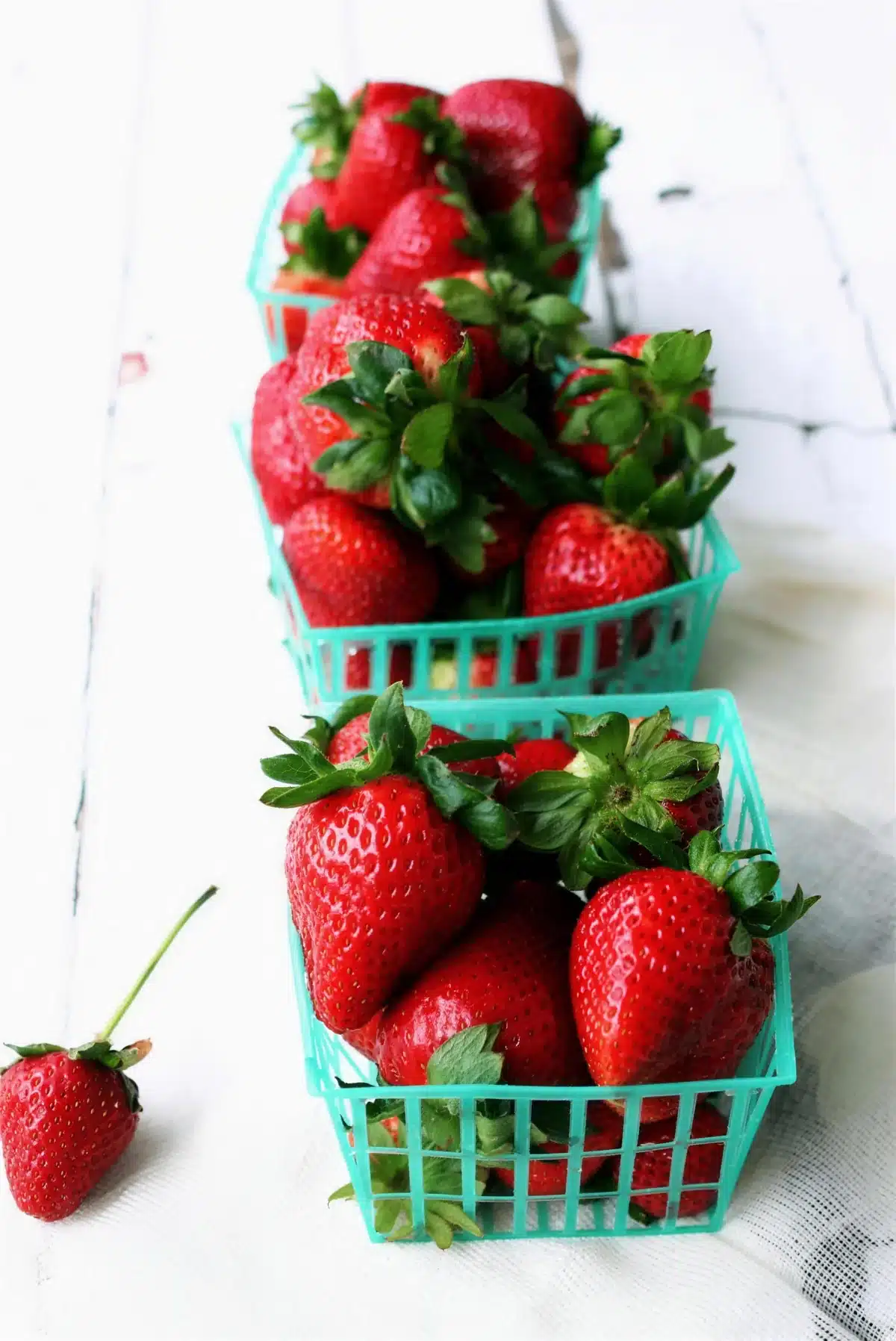 Ripe red fruit in green produce baskets on a white painted table