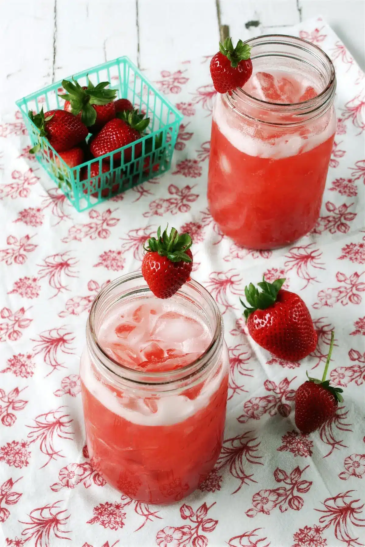Strawberry syrup topped with sparkling water in two jars over crushed ice
