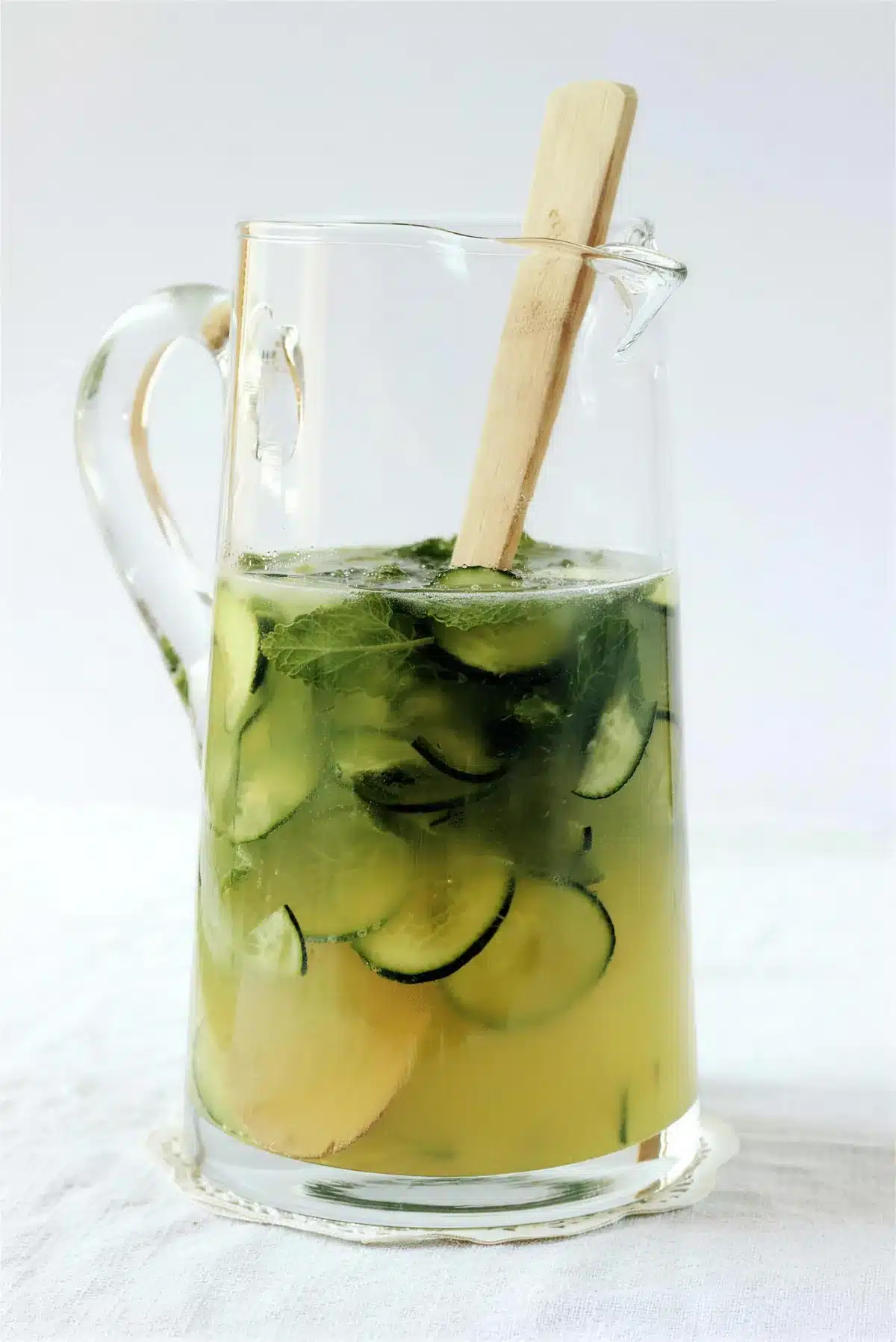 Gin lemonade in a glass pitcher with cucumber slices and a wooden muddler