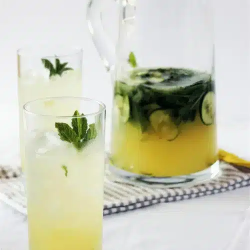 Gin lemonade in a tall glass beside a full pitcher on a striped cloth