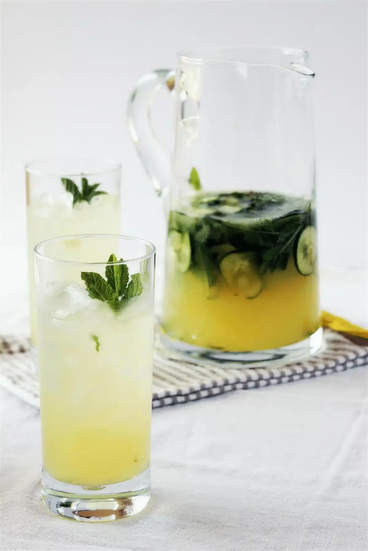 Gin lemonade in a tall glass beside a full pitcher on a striped cloth