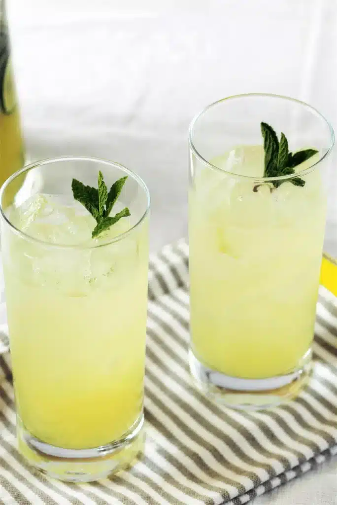 Two tall glasses over ice with mint tips on a striped napkin